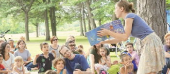 adult reading a book to families outside at a park